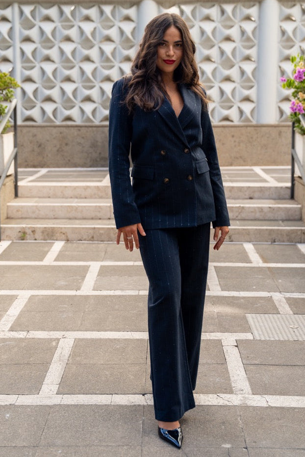 Woman in a dark suit standing on a tiled patio with decorative wall and plants in the background