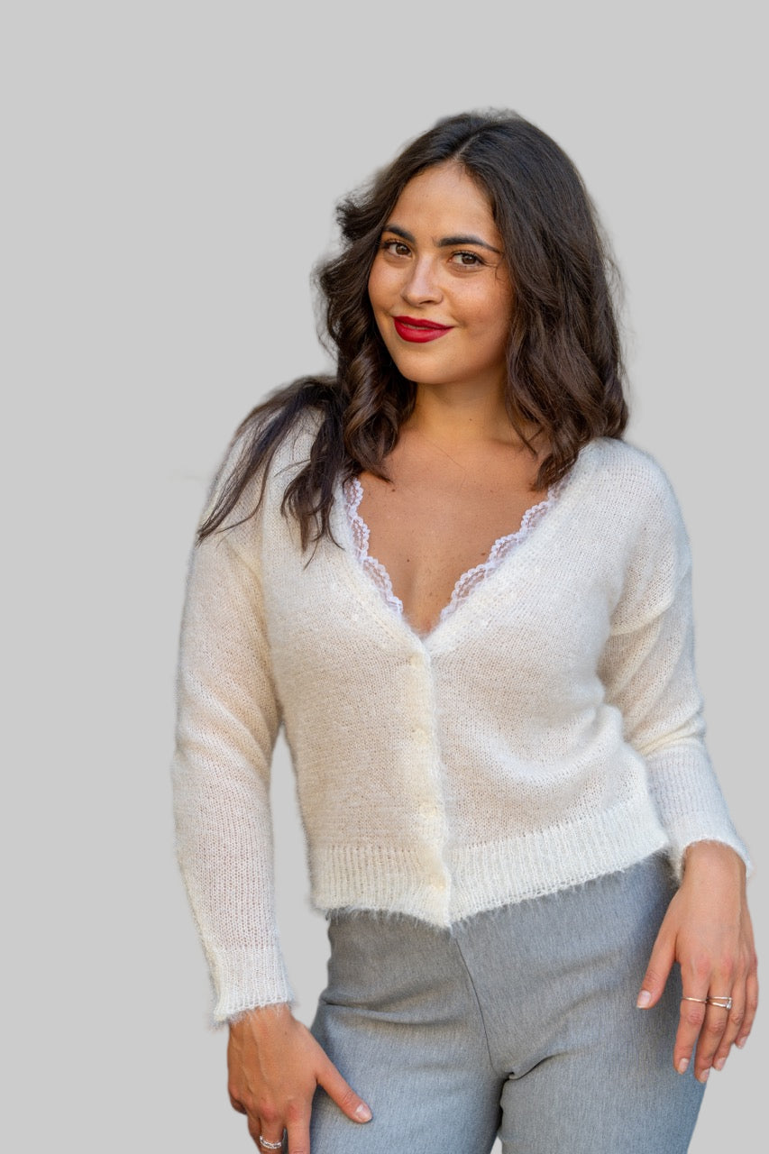 Woman wearing a white cardigan with lace trim in an outdoor setting